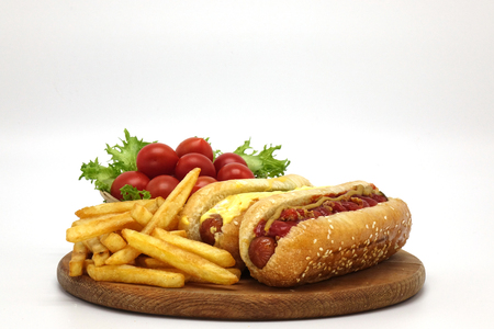 Hot dogs and French fries on white background. Sausages with tomato sauce and cherry tomatoes on a wooden Board.の写真素材