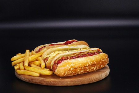 Hot dogs and French fries on black background. Sausages with tomato sauce on wooden Board.