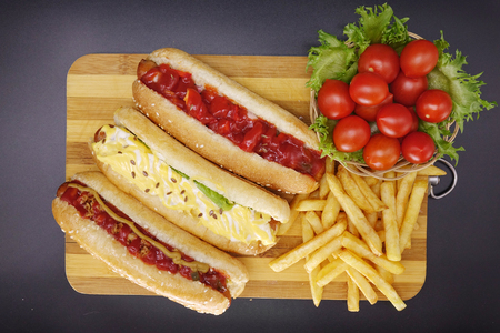 Hot dogs and French fries on black background. Sausages with tomato sauce and cherry tomatoes on a wooden Board.の写真素材