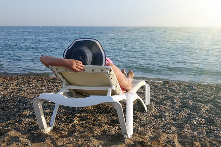 Woman in hat relaxing on the beach looking at the sea. Holiday season. Copy space.の写真素材