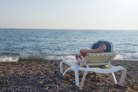 Woman in hat relaxing on the beach looking at the sea. Holiday season. Copy space.の写真素材