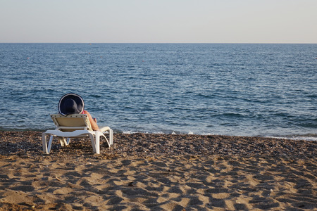 Woman in hat relaxing on the beach looking at the sea. Holiday season. Copy space.の写真素材