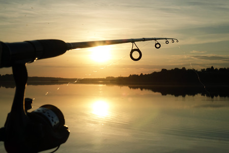 Silhouette of hands of fisherman with fishing spinning rod on sunset backgroundの写真素材