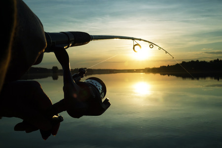 Silhouette of hands of fisherman with fishing spinning rod on sunset backgroundの写真素材
