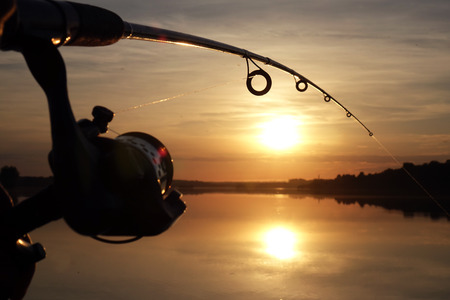 Silhouette of hands of fisherman with fishing spinning rod on sunset backgroundの写真素材