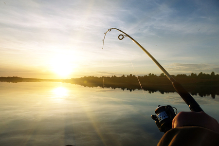 Silhouette of hands of fisherman with fishing spinning rod on sunset backgroundの写真素材