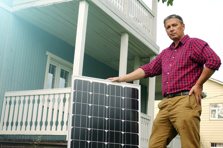Solar panels in the hands of men . Energy production technologies. Wooden house background.の写真素材