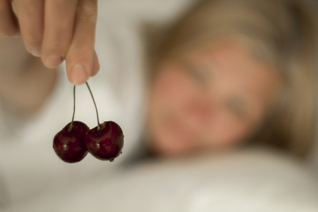 woman lying in bed and eating cherriesの写真素材