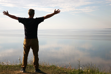 A man stands on top of a mountain and sees the view of nature. The tourist raises his hands and enjoys the fresh air. A man enjoying free happiness in a beautiful landscapeの写真素材