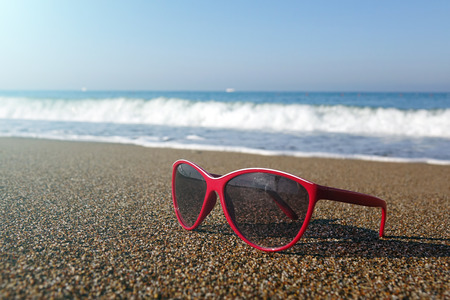 Red sunglasses on the sand at the beach, summer time