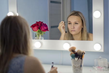 Woman doing makeup, looking in the mirror. Makeup in the daytime is prepared before going to a party.の写真素材