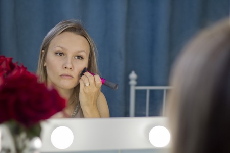 Woman doing makeup, looking in the mirror. Makeup in the daytime is prepared before going to a party.の写真素材