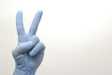 Surgeon's hand in blue medical glove showing OK sign isolated backgroundの写真素材