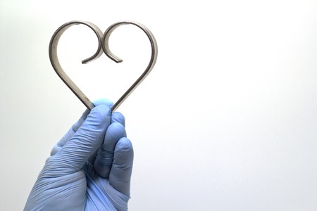 The surgeon's hand in a blue medical glove holds an iron heart . The concept of health. Isolated background.の写真素材