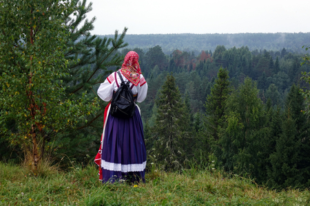 Girl in a traditional folk costume in nature, looking into the distance. Green pine forestの写真素材