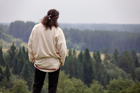 A young man in a traditional folk costume in nature, looking into the distance. Green pine forestの写真素材