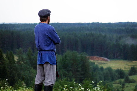 A young man in a traditional folk costume in nature, looking into the distance. Green pine forestの写真素材