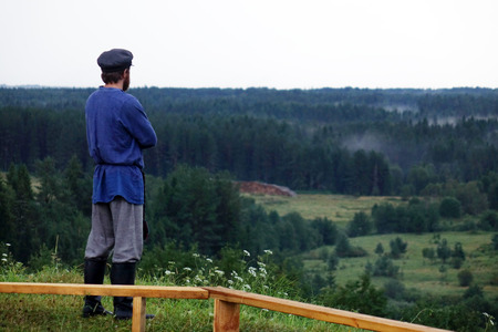 A young man in a traditional folk costume in nature, looking into the distance. Green pine forestの写真素材