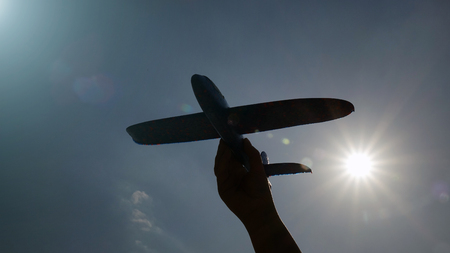 Silhouette of a model airplane in the hand in the Sunny sky. The concept of travel and transport. Dream about vacationの写真素材