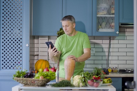 A man in the kitchen prepares vegetarian dishes. Looks up a recipe on the tablet display.の写真素材
