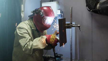 Welder in the mask. The metal product is welded by welding machine