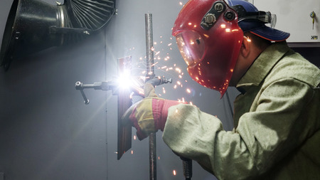 Welder in the mask. The metal product is welded by welding machine