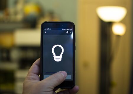 Smart home: man controlling lights with app on his phone. electric concept.の写真素材