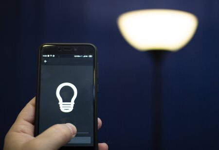 Smart home: man controlling lights with app on his phone. electric concept.の写真素材