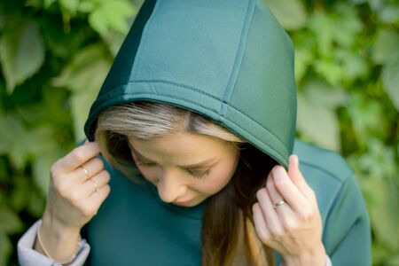 Portrait of a beautiful girl in a green coat on a background of ivy .Woman enjoy Sunny day outdoors. The concept of the fall season. Catch the last rays of the sun. A feeling of warmth.の写真素材