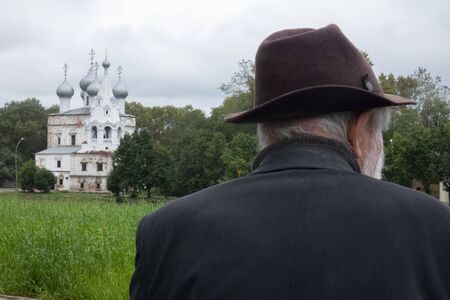 An old man in a hat sits on the background of an Orthodox Church. lonelinessの写真素材