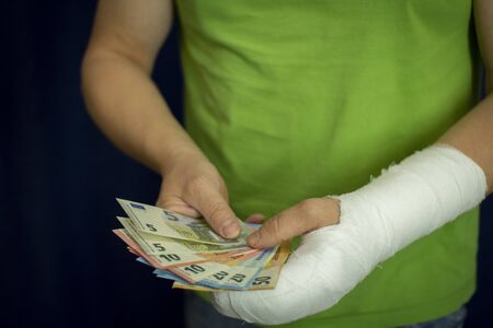 A man with an arm in a cast keeps money from the cost and expense of emergency medical care in a hospital . Paid medicine..Man's hand in bandages after surgery.の写真素材