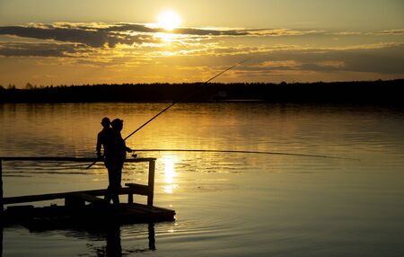 Two silhouettes of fishermen on the lake during sunsetの写真素材