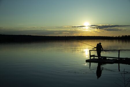 Two silhouettes of fishermen on the lake during sunsetの写真素材