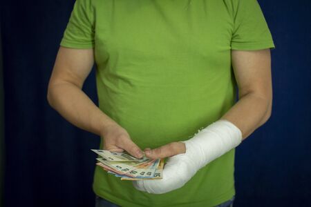 A man with an arm in a cast keeps money from the cost and expense of emergency medical care in a hospital . Paid medicine..Man's hand in bandages after surgery.の写真素材