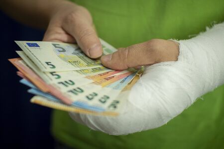 A man with an arm in a cast keeps money from the cost and expense of emergency medical care in a hospital . Paid medicine..Man's hand in bandages after surgery.の写真素材