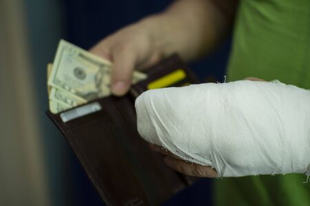 A man with an arm in a cast counted out money from the cost and expenses of emergency medical care at the hospital . Paid medicine..Man's hand in bandages after surgery.の写真素材