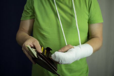 A man with an arm in a cast counted out money from the cost and expenses of emergency medical care at the hospital . Paid medicine..Man's hand in bandages after surgery.の写真素材