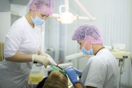A female dentist and her assistant in a white uniform examine a patient. Medicine, Dentistry, orthodontic concept.の写真素材