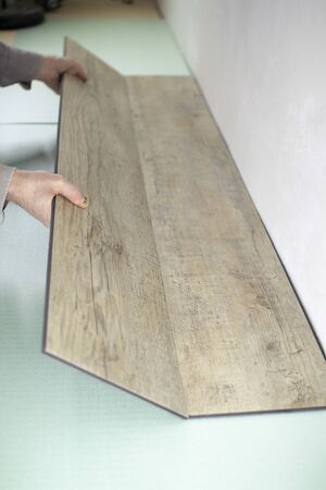 Vinyl laminate. Laying of the floor covering. A worker installing a new vinyl tile on the floorの写真素材