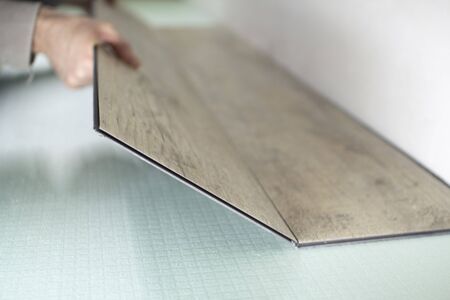 Vinyl laminate. Laying of the floor covering. A worker installing a new vinyl tile on the floorの写真素材