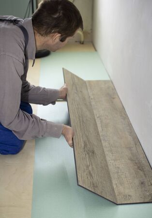 Vinyl laminate. Laying of the floor covering. A worker installing a new vinyl tile on the floorの写真素材