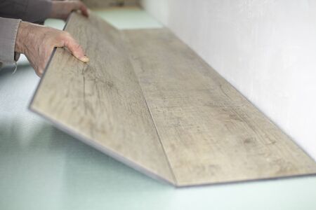 Vinyl laminate. Laying of the floor covering. A worker installing a new vinyl tile on the floorの写真素材