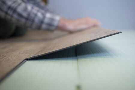 Vinyl laminate. Laying of the floor covering. A worker installing a new vinyl tile on the floorの写真素材