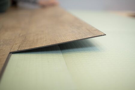 Vinyl laminate. Laying of the floor covering. A worker installing a new vinyl tile on the floorの写真素材