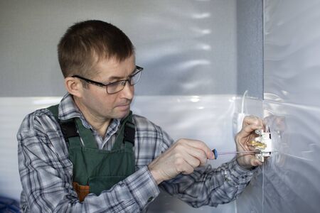 The electrician uses a screwdriver to secure the socket to the wall.の写真素材