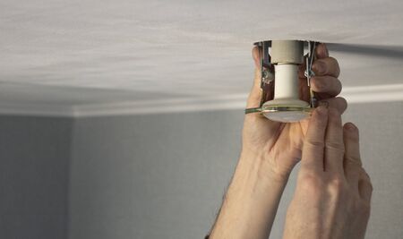 Installing spot light, hand inserts the lamp into the ceiling, close-up. The electrician inserts a...