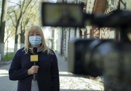 A female journalist in a protective medical mask is reporting in a deserted city.の写真素材