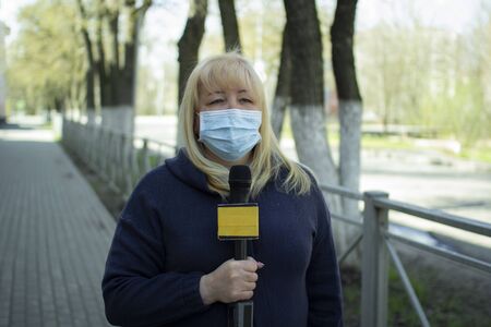 A female journalist in a protective medical mask is reporting in a deserted city.の写真素材