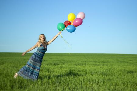 Girl with balloons in the field. Solar and positive energy of nature. Young beautiful woman on the grass in the Park.の写真素材