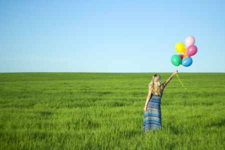 Girl with balloons in the field. Solar and positive energy of nature. Young beautiful woman on the grass in the Park.の写真素材